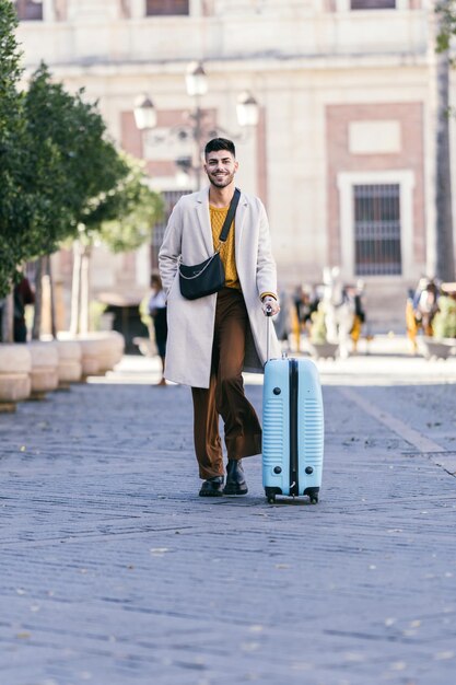 Vertical photo of a stylish man with coat carrying a suitcase on the street