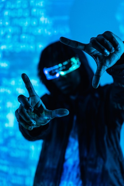 Vertical photo with blue neon light of a futuristic man gesturing while wearing vr goggles