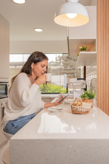 Vertical photo of a woman having breakfast and using the mobile in a new kitchen