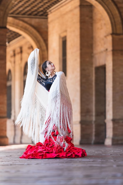 Vertical photo of a woman in red flamenco dress dancing in Spain square in Seville