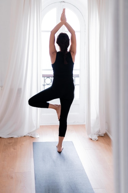 Vertical photo of woman in uniform sportswear top leggings Doing yoga asana exercise meditating at home near window on a mat Healthy sport