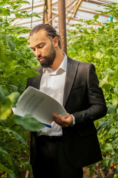 Vertical photo of young businessman checking notes at the greenhouse