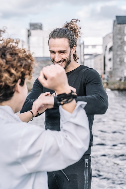 Vertical photo of a young couple arguing and fighting with funny expression with buildings and blurred sea 