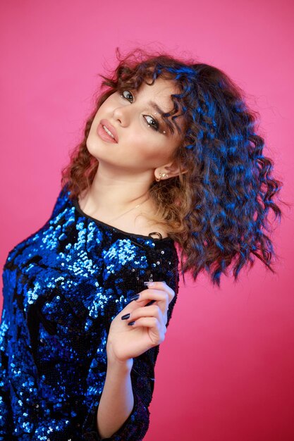 Vertical photo of young lady shaking her hair and looking at the camera on pink background High quality photo