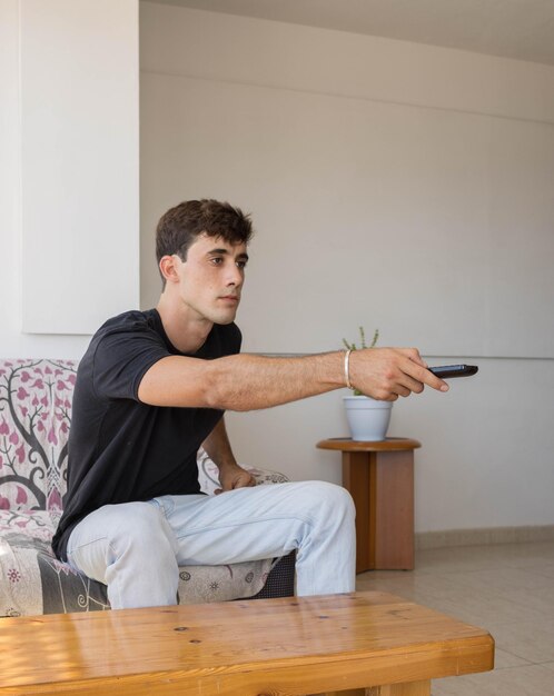 Vertical photo of a young man sitting alone on the sofa at home while turning on the television