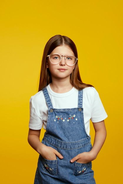 vertical photo of young teen girl in glasses and denim stands confidently in front of a bright