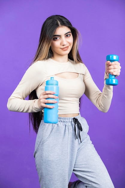 Foto verticale della giovane donna in possesso di una bottiglia d'acqua giovane ragazza in forma stand su sfondo viola foto di alta qualità