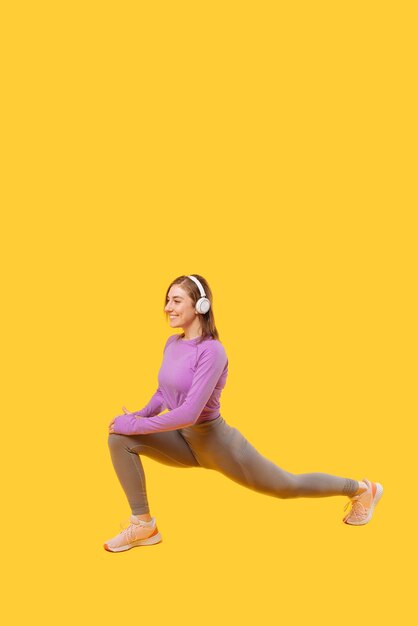 Vertical photo of a young woman performing lunges while listening to the music