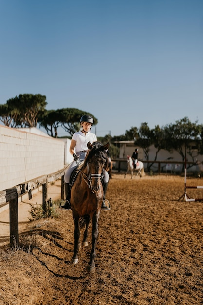 乗馬場で茶色の馬と一緒にウォーミングアップする若い女性の縦の写真