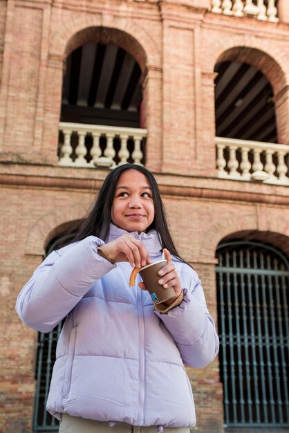 Vertical photography of teenager enjoying eating churros with chocolate at the street