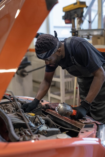 Premium Photo  Vertical portrait of african-american male mechanic looking  under hood while repairing car in auto shop