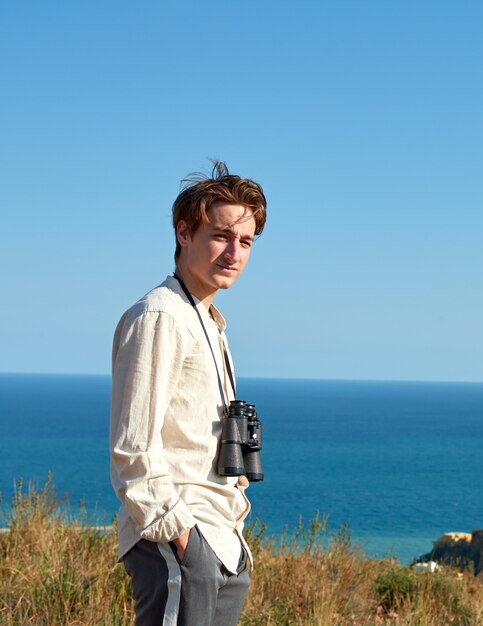 A vertical portrait of an attractive young man with binoculars hanging around his neck