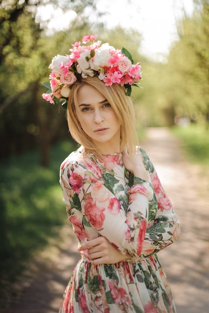 Vertical portrait of beautiful blonde woman dressed in flower dress and pink wreath