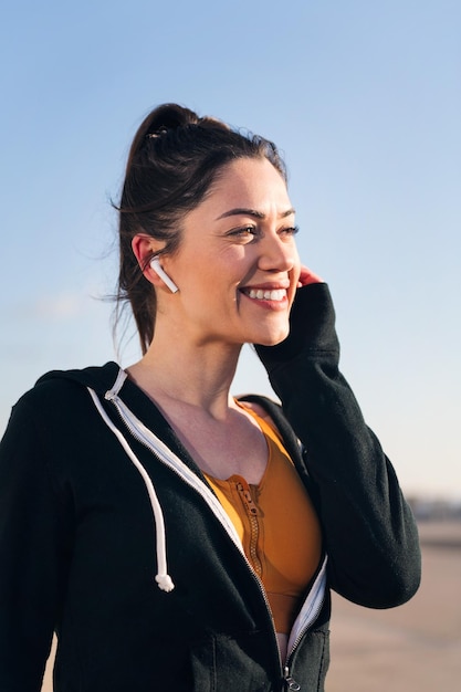 vertical portrait of a beautiful sportswoman using earphones outdoors in a sunny day concept of technology and sportive lifestyle