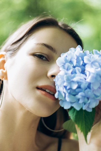 Vertical portrait of beautiful young woman standing posing in park with blooming flowers Hydrangea