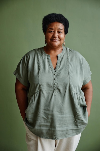 Vertical portrait of black senior woman smiling at camera while standing against green background