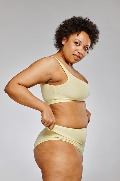 Vertical portrait of black woman wearing underwear and looking at camera against grey background bod
