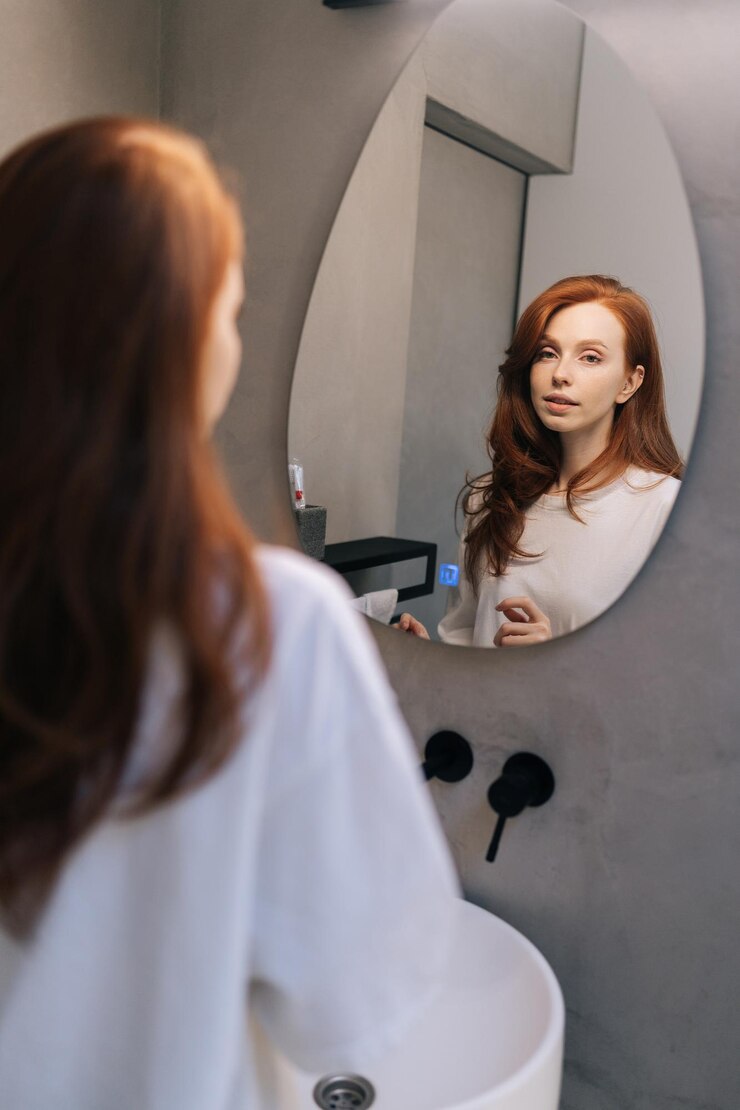 Photo vertical portrait of charming woman in casual clothes preening do morning routine touch her hair standing in front of mirror smiling admire herself feels satisfied