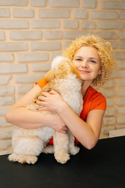 Vertical portrait of cheerful female groomer hugging curly\
labradoodle dog after haircutting at grooming salon attractive\
woman pet hairdresser doing professional care in veterinary spa\
clinic