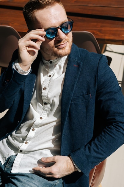 Photo vertical portrait of confident young man in sunglasses wearing stylish suit wear sitting in armchair looking away out window