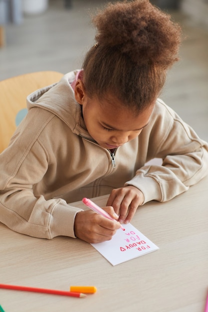 Ritratto verticale di una simpatica ragazza afro-americana che fa una carta fatta a mano come regalo per la festa del papà, copia spazio