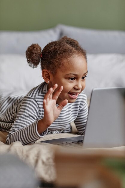 Photo vertical portrait of cute african-american girl waving at camera while video chatting with friends