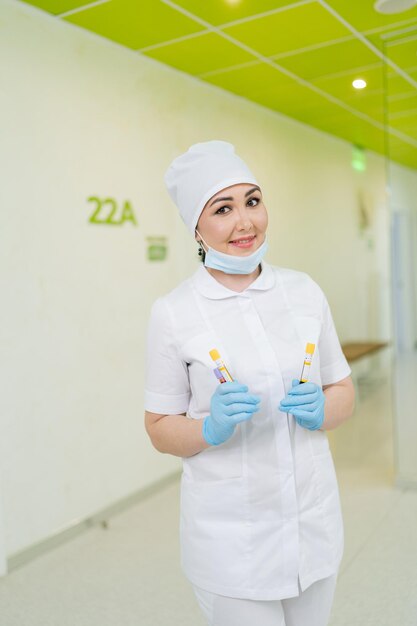 Photo vertical portrait of friendly female nurse in medical uniform holding blood test tubes standing on