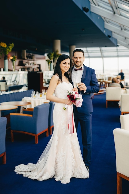 Vertical portrait of good looking female bride and bridegroom hold glasses with champagne celebrate their special occasion have pleased expressions look directly into camera Celebration concept