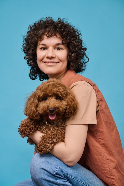 Vertical portrait of happy owner posing with her pet against blue background