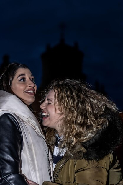 Vertical portrait of a laughing female couple hugging on the street at night