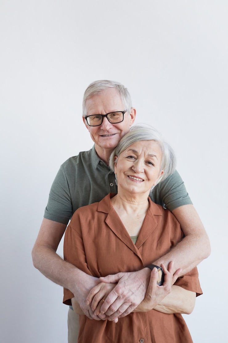 Photo vertical portrait of loving senior couple embracing and looking at camera while standing against white background