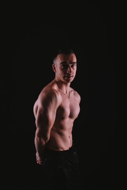 Vertical portrait of muscular young man standing over dark background