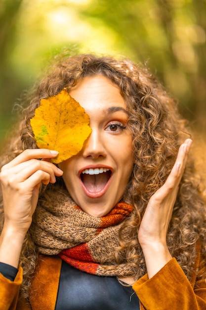 写真 黄色い葉の中に隠れている遊び心のある女性の垂直の肖像画