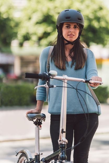 通りで自転車の横に立っているヘルメットを持つ若い女性の縦の肖像画