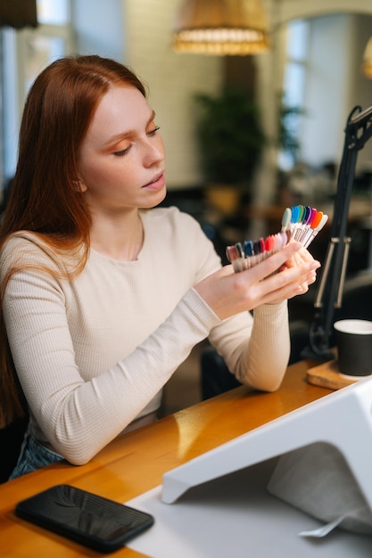 Vertical portrait of pretty young woman client choosing colour from colourful nails tips in manicure salon