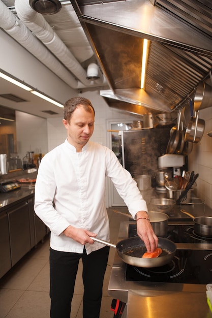 Vertical portrait of a professional chef frying salmon at the restaurant