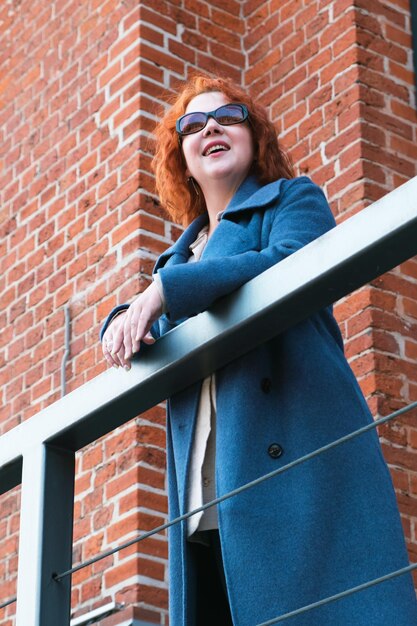 Vertical portrait of redhaired woman in full growth in a blue coat