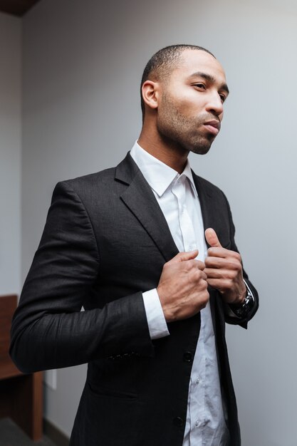 Vertical portrait of Serious African man preparing in hotel room and looking away