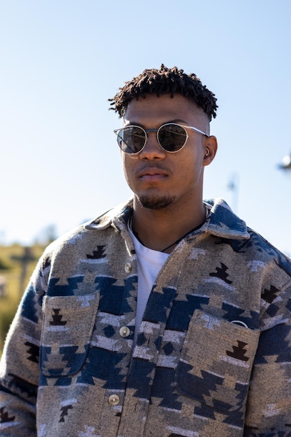 Vertical portrait of a serious black Latino man with beard and sunglasses looking at the camera in summertime