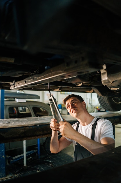 Vertical portrait of serious handsome professional male car mechanic in uniform standing in inspection pit and working with tool Concept of car service repair and maintenance