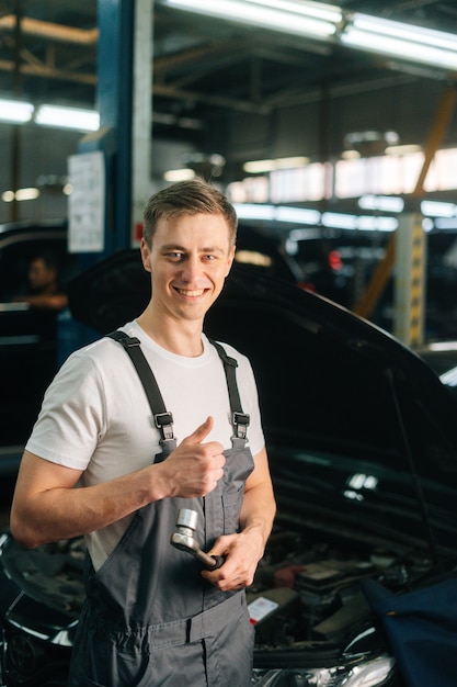 Vertical portrait of smiling handsome young mechanic male wearing uniform holding special key