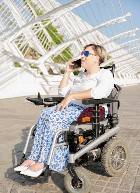 Vertical portrait of a smiling woman sitting in an electric wheelchair talking on a mobile phone