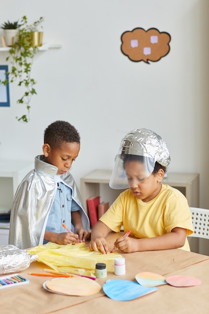 Vertical Portrait of two African-American boys playing astronauts and making space suits while enjoying art and craft lesson in preschool or development center