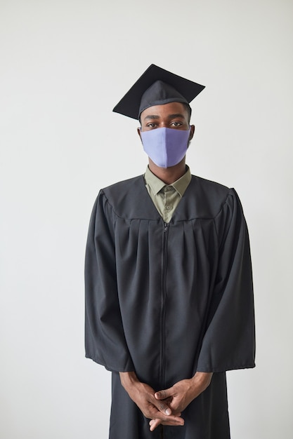 Vertical portrait of young African American college graduate wearing mask indoors