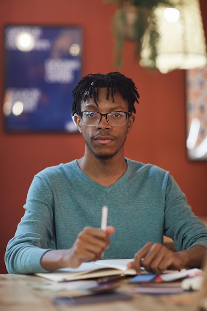 Vertical portrait of young African-American man while sitting at table against red wall in cafe