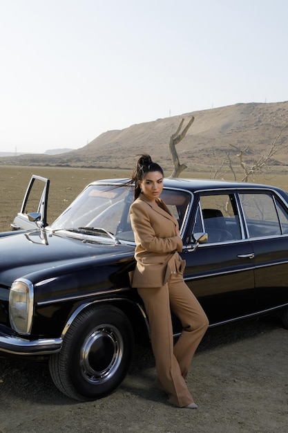 Vertical portrait of young beautiful model lean on oldschool car at desert High quality photo