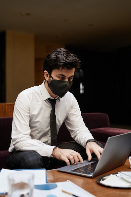 Vertical portrait of young businessman wearing mask while working in hotel lobby