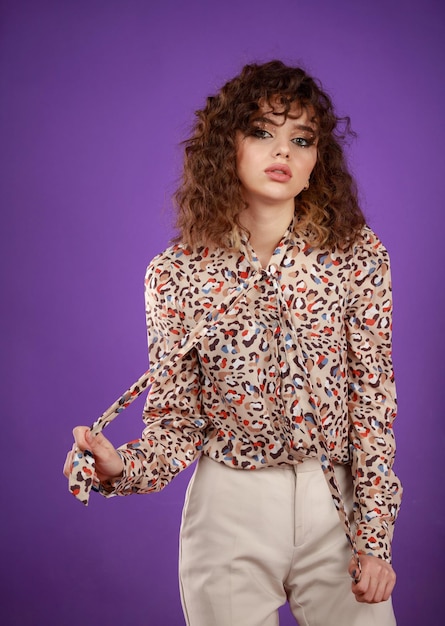 Vertical portrait of young curlyhaired girl stretching her shirt and stand on purple background High quality photo