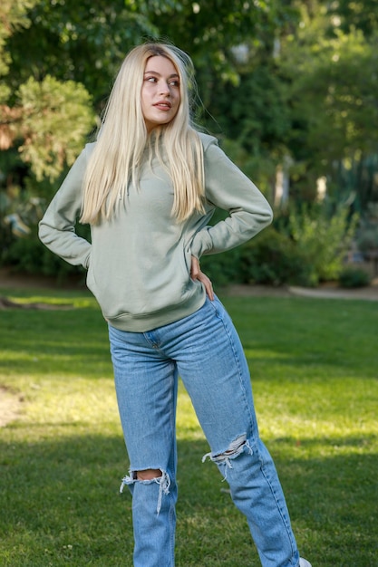 Vertical portrait of young cute lady standing at the park and put her hands into her pocket