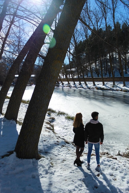 눈 덮인 배경에서 얼음 강을 바라보는 젊은 인종 커플의 세로 초상화. 여행 및 휴가 개념입니다. 발렌타인 데이 축하